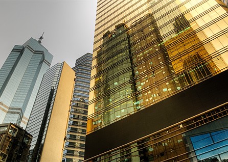 Skyscrapers with glass facades reflecting the surrounding cityscape under a cloudy sky.